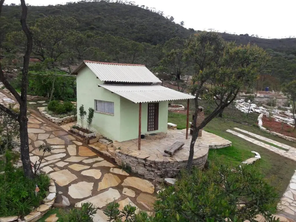 Chalé verde com varanda de pedra, churrasqueira ao lado e mata ao fundo